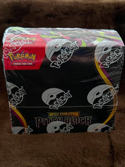 A sealed Pokémon Mega Evolution Pitchblack trading card game booster box wrapped in clear plastic, photographed on a brown textured surface.