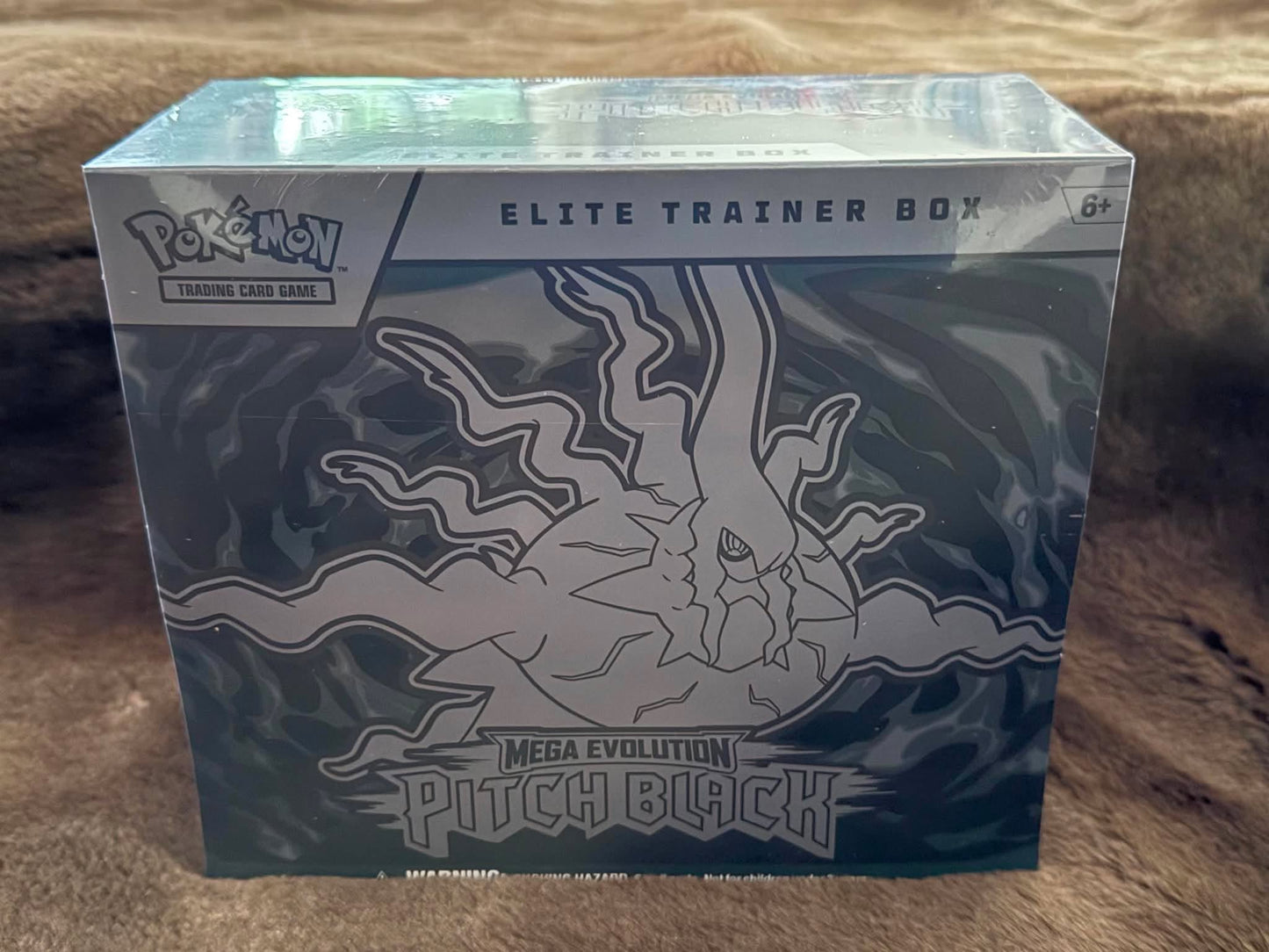 Pokémon Trading Card Game Elite Trainer Box for Pitch Black from the Mega Evolution expansion, sealed in its original plastic shrink wrap and photographed on a brown textured surface.