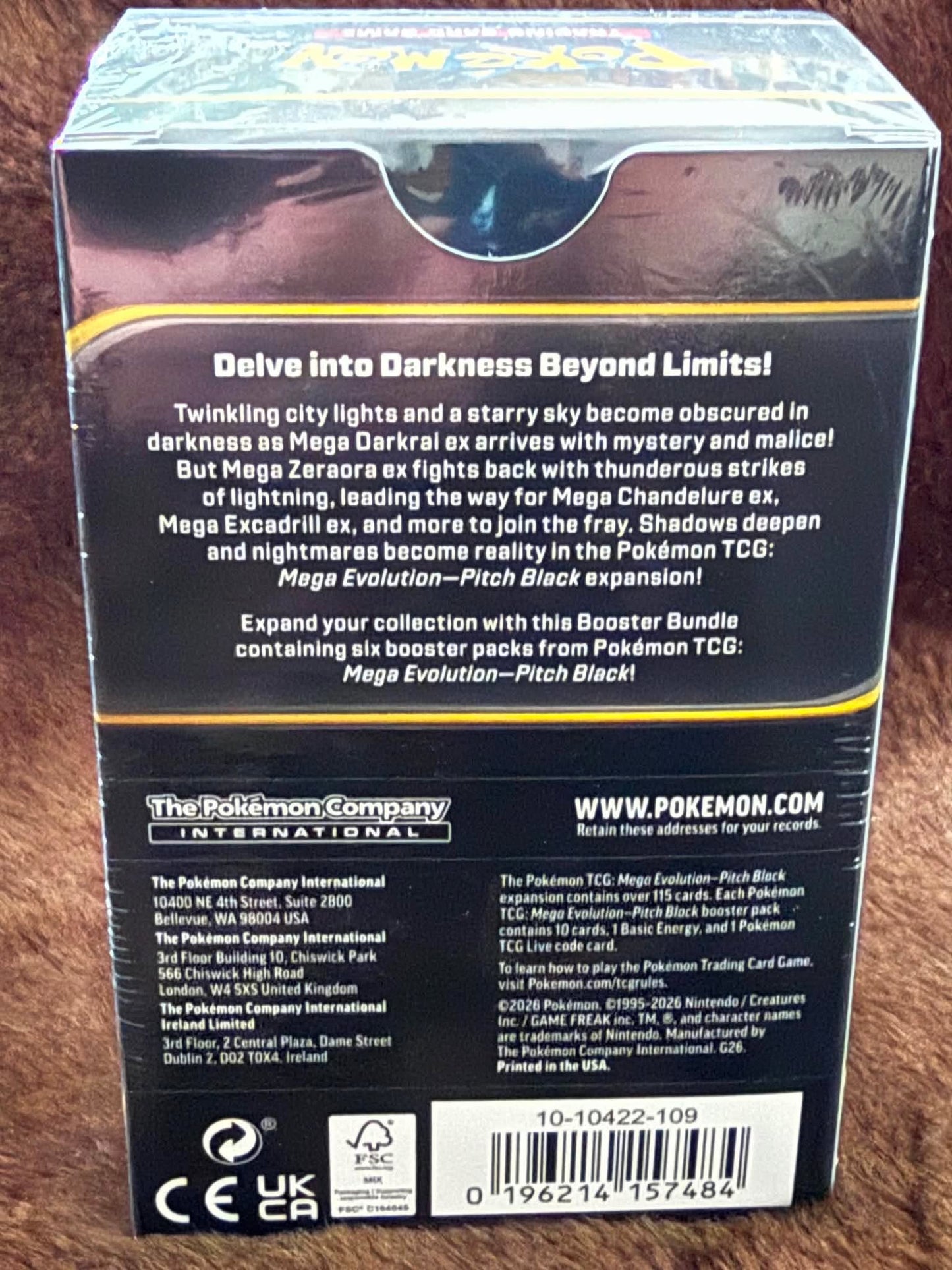 Back of a Pokémon TCG booster box for Pokémon Company International, featuring product description, website, barcodes, and certification logos on a dark background.