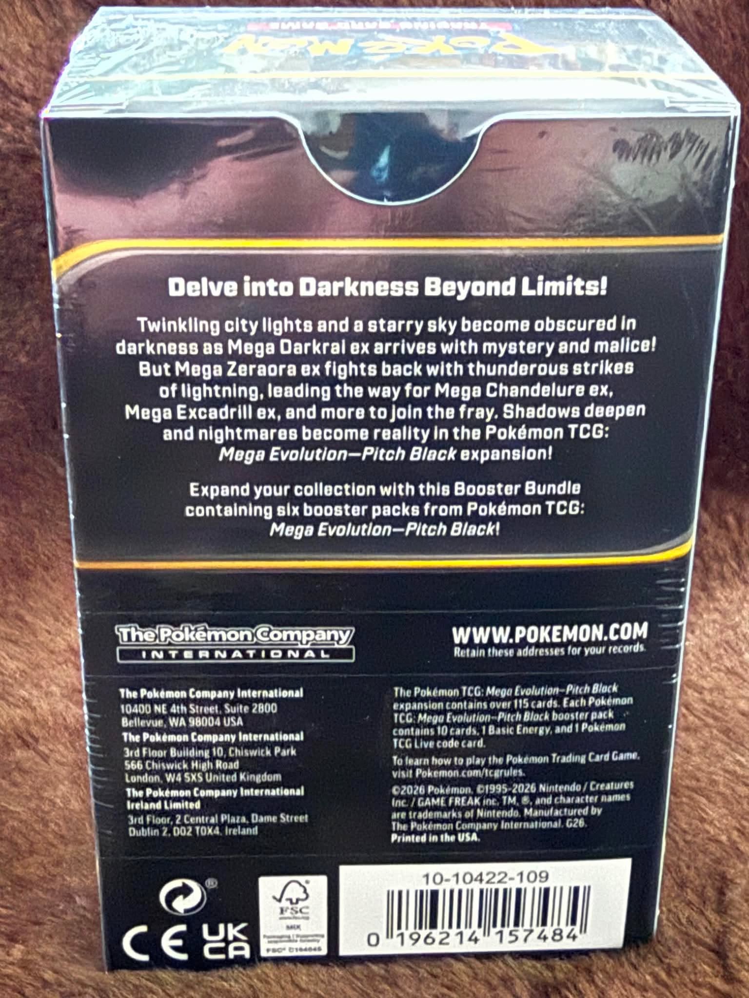 Back of a Pokémon TCG booster box for Pokémon Company International, featuring product description, website, barcodes, and certification logos on a dark background.